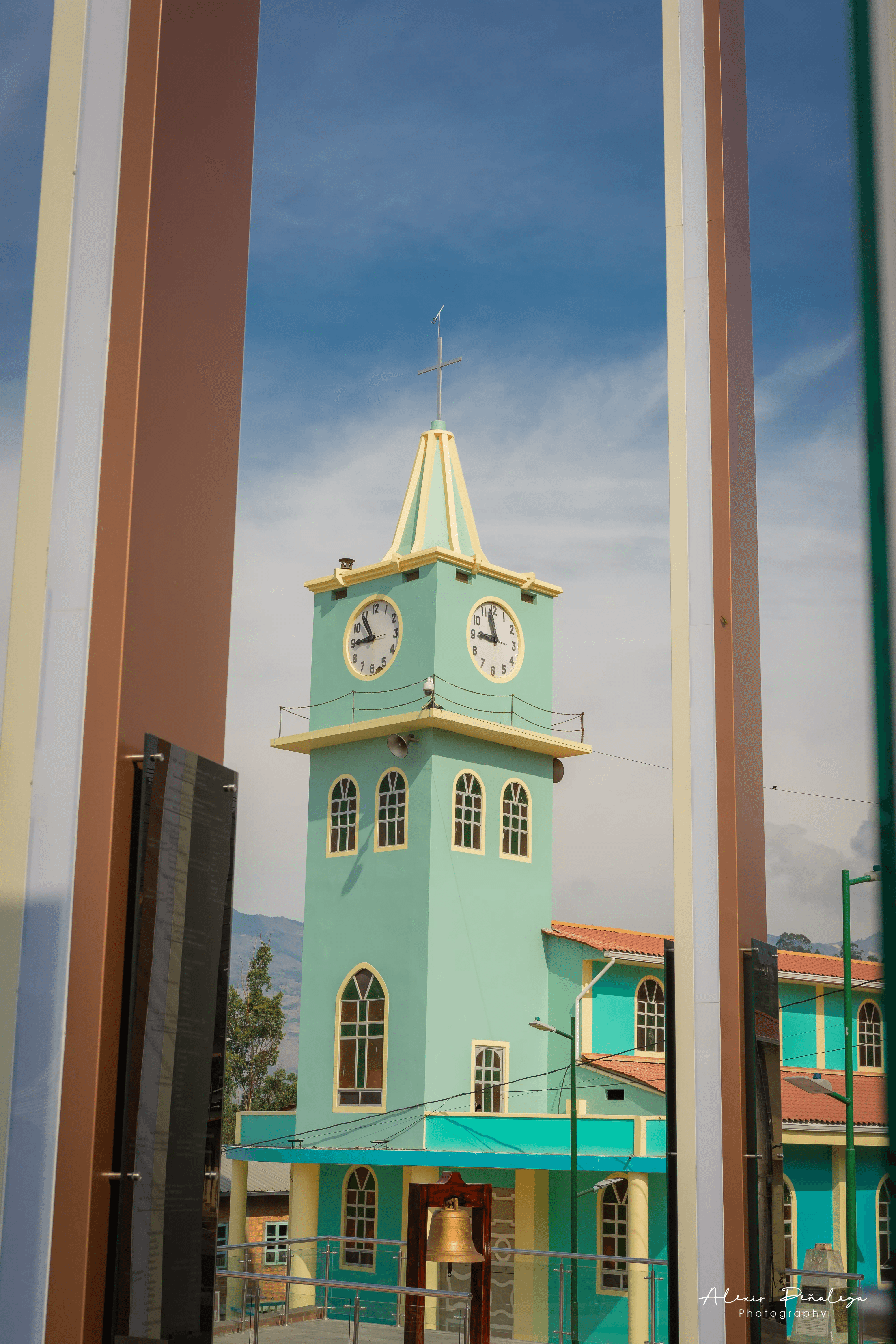 Torre de la iglesia y campana de bronce vistas entre las columnas del parque
