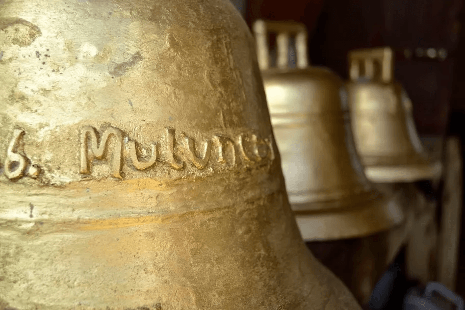 Acercamiento macro a una campana dorada con la palabra Muluncay grabada rústicamente en relieve