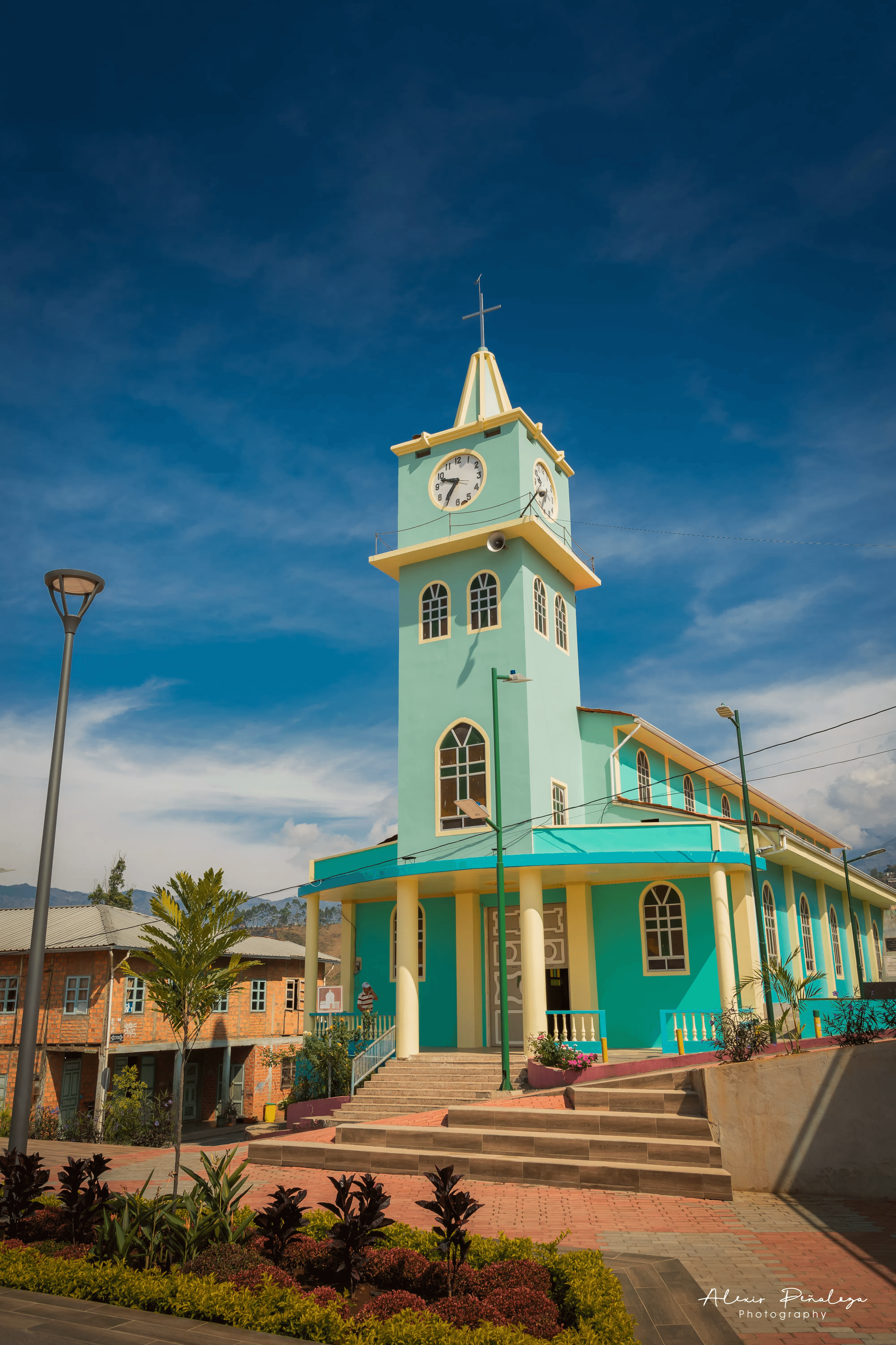 Toma angular de la iglesia turquesa parroquial y su torre del reloj desde la acera