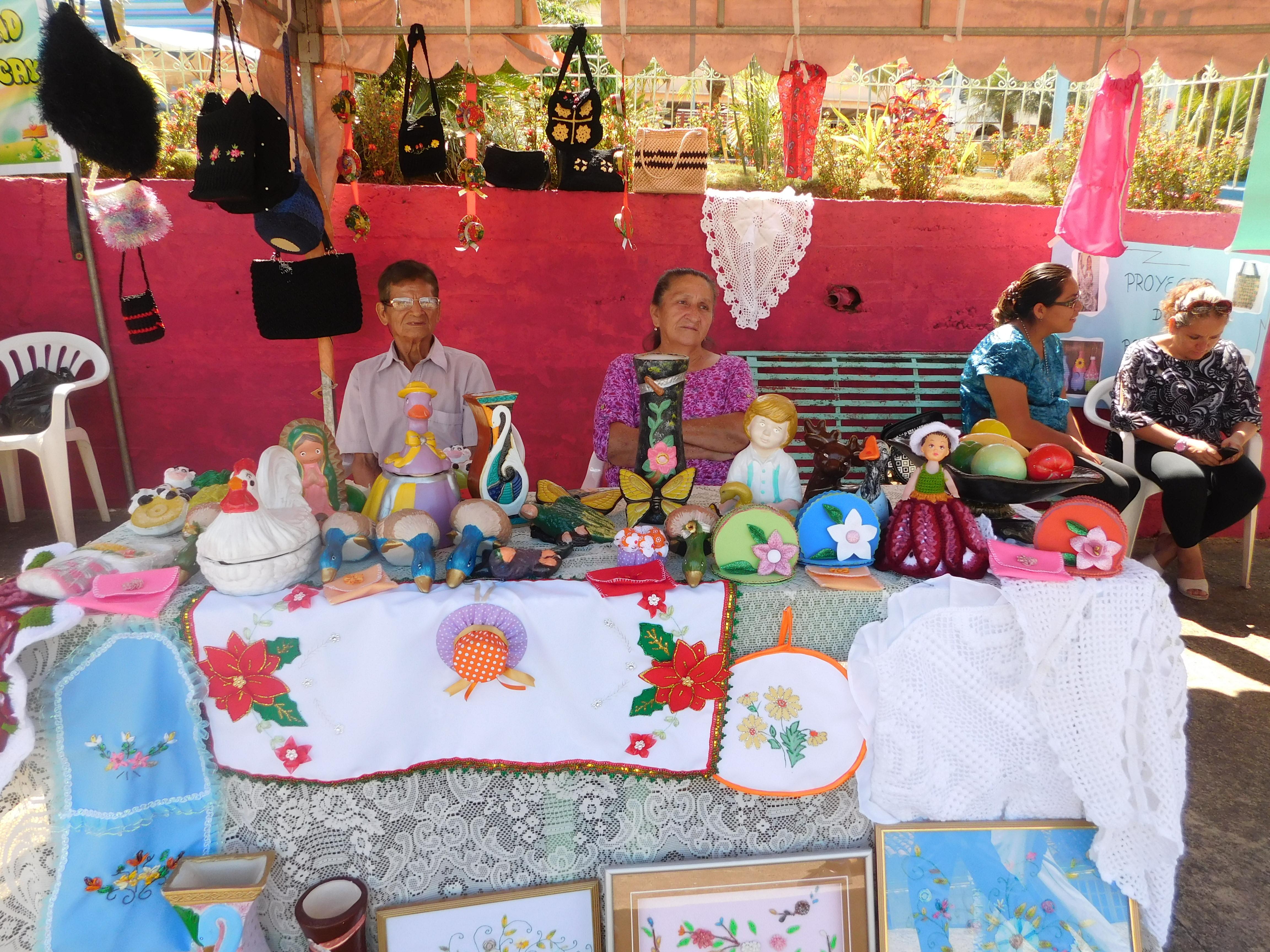 Pareja de artesanos exhibiendo bordados, figuras de cerámica y manualidades en una casa abierta