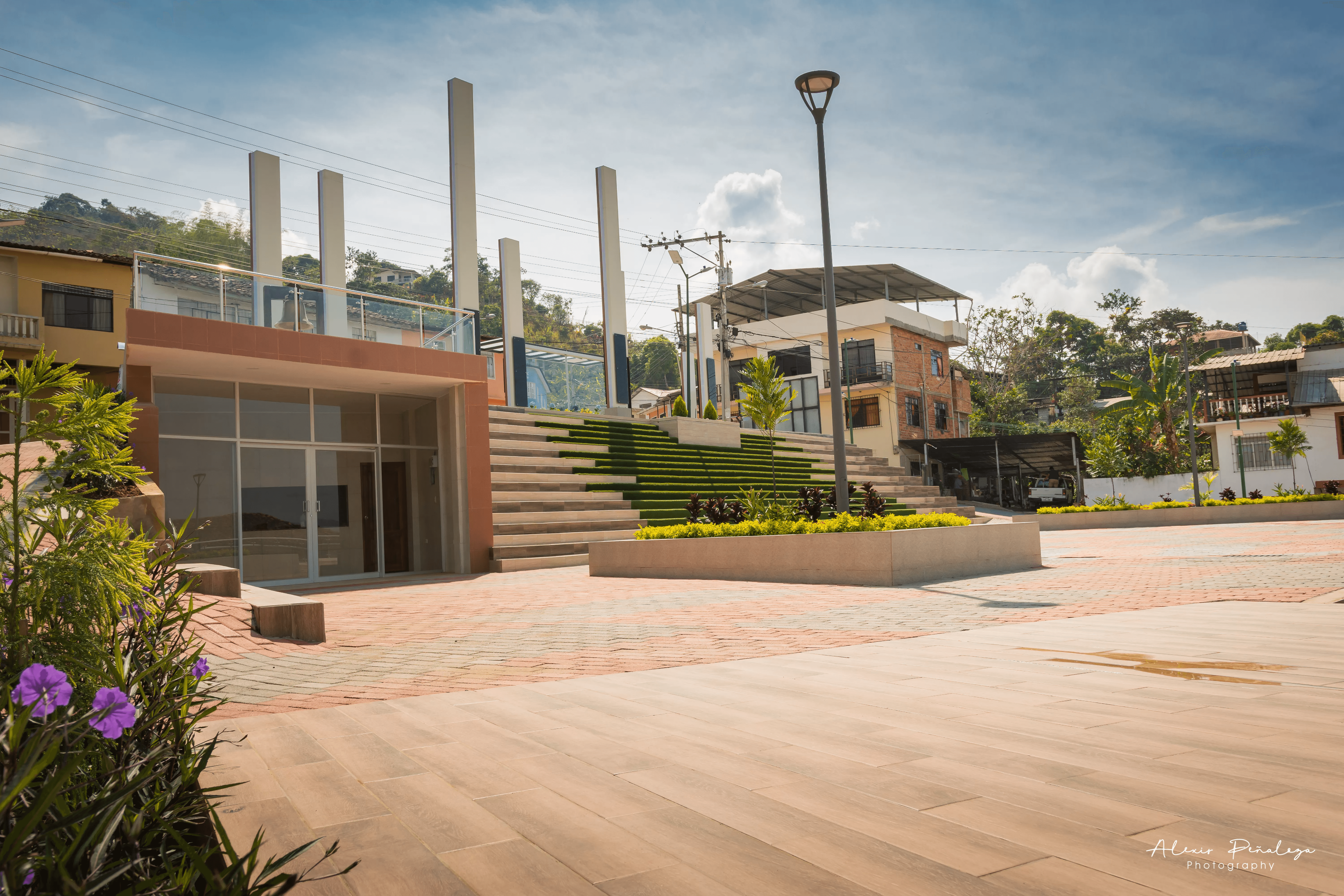 Amplia plaza peatonal esquinera con griderío verdoso y un edificio moderno con balcón