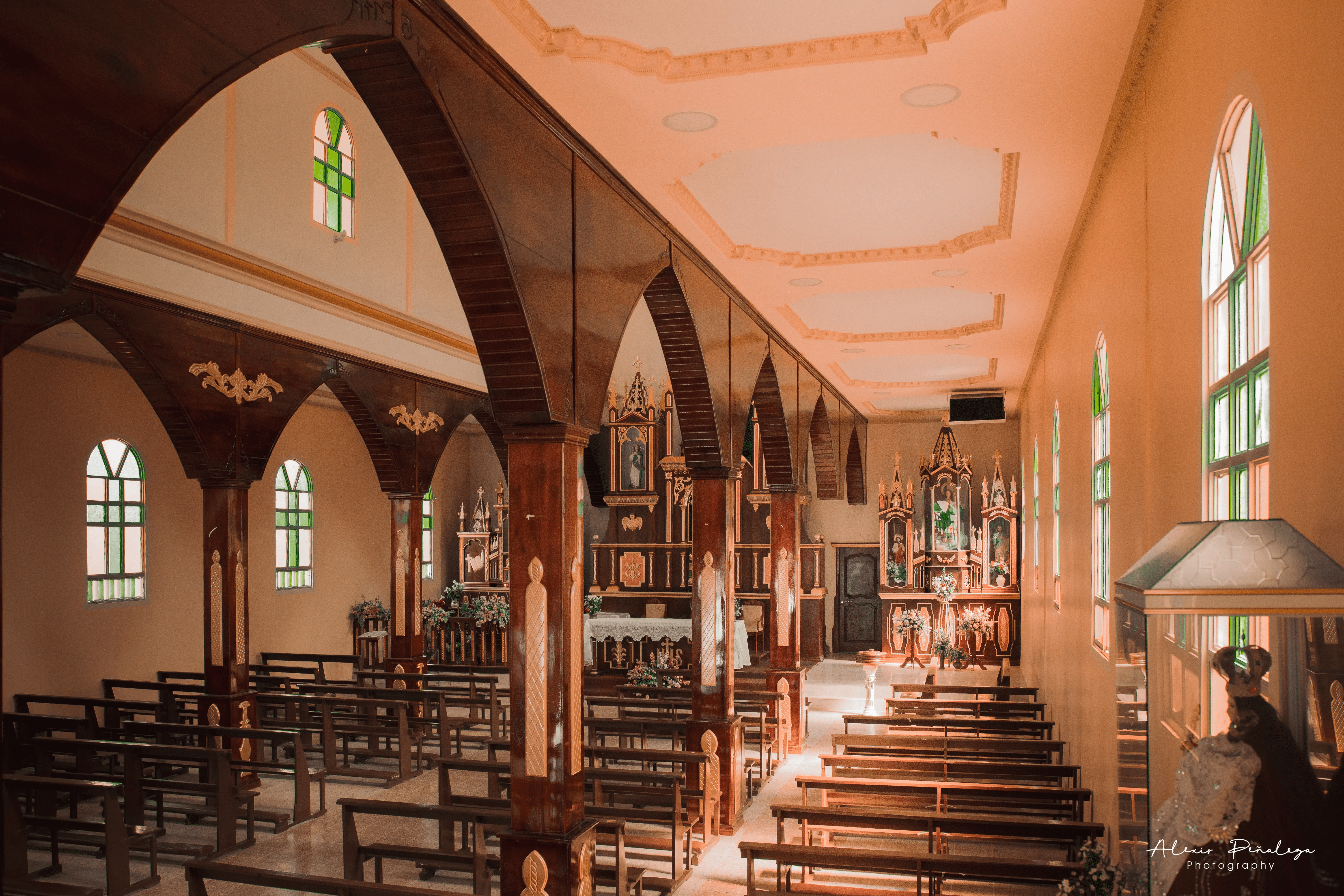 Interior de la iglesia desde un ángulo lateral, con bancas, altar y urna religiosa